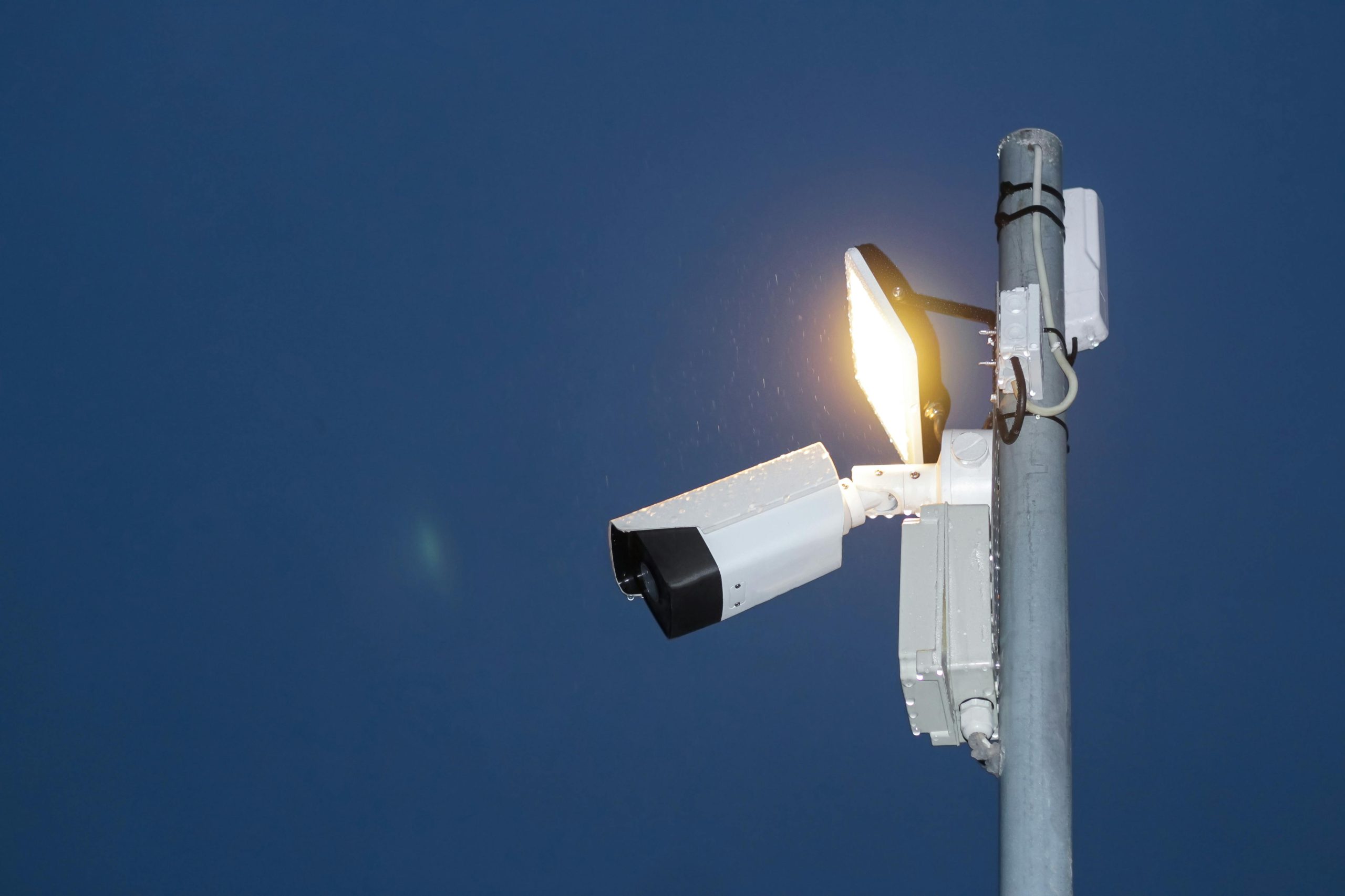 Picture of a ANPR camera attached to a large pole against a blue background at night.